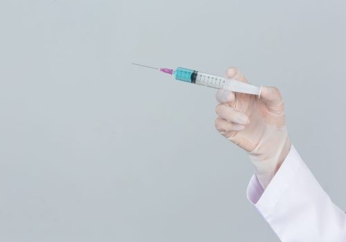 Young doctor is  holding  hypodermic syringe with rubber gloves on gray background.